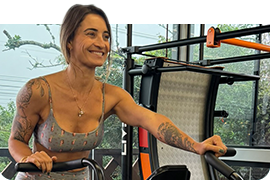 Mulher sorrindo enquanto se exercita em aparelho de cardio em academia moderna com equipamentos ao fundo